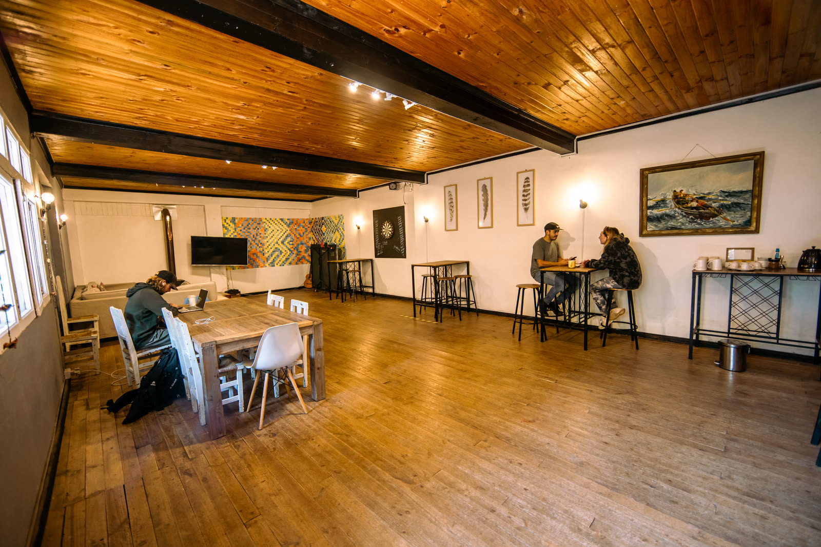 Sala multiuso de techo de madera con mesa de comedor larga, televisor y tablero de dardos